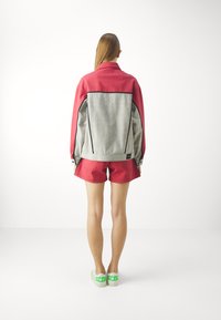 Red and gray color-blocked jacket with a structured design, paired with red shorts. Shoes are white with green text. Back view.