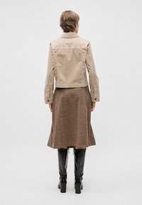 Veste beige cropped avec col, assortie à une jupe brown texturée évasée et des bottes noires à talons blocs mi-mollet.