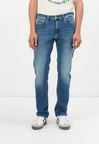 Jeans din denim albastru cu o croială dreaptă, cinci buzunare și un efect subtil de decolorare. Asortați cu adidași albi cu dungi negre.
