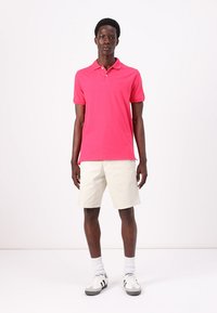 Lys pink polo-shirt med krave og korte ærmer, parret med lyse beige shorts. Hvide sportssko fuldender outfittet.