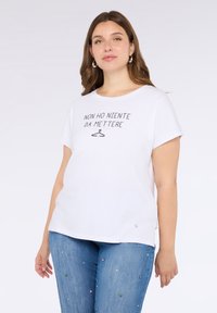 Camiseta blanca de algodón con mangas cortas, que presenta una frase impresa y un gráfico de perchero. Combinada con jeans azul claro adornados con pequeños gemas.