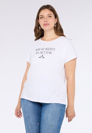 Witte katoenen t-shirt met korte mouwen, voorzien van een gedrukt zinsdeel en een hangerafbeelding. Gecombineerd met lichtblauwe jeans versierd met kleine edelstenen.