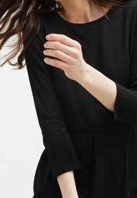 Czarna sukienka z rękawami o długości trzech ćwierć, gładka faktura i dopasowany gorset prowadzący do rozkloszowanej spódnicy. Minimalistyczny design, brak widocznych wzorów.