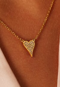 Gouden ketting met een hartvormige hanger versierd met heldere rhinestones, tegen een achtergrond van gladde huid.