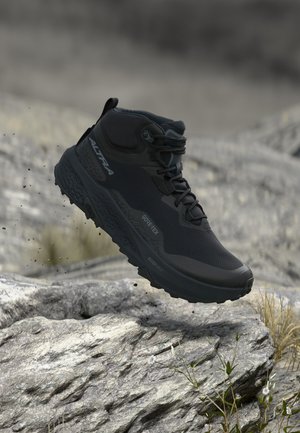 Schwarzer High-Top-Wanderschuh mit Schnürsenkeln, über felsigem Gelände schwebend, zeigt Gore-Tex- und Altra-Branding an der Seite.