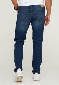 Mörkblå denimjeans med rak passform, med bruna sömmar och två bakfickor, bärs med vita sportskor.