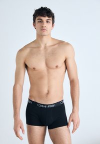 Schwarze Calvin Klein Boxershorts mit einem weichen Bund, präsentiert an einem Modell ohne Shirt. Der Stoff wirkt glatt und körperbetont.