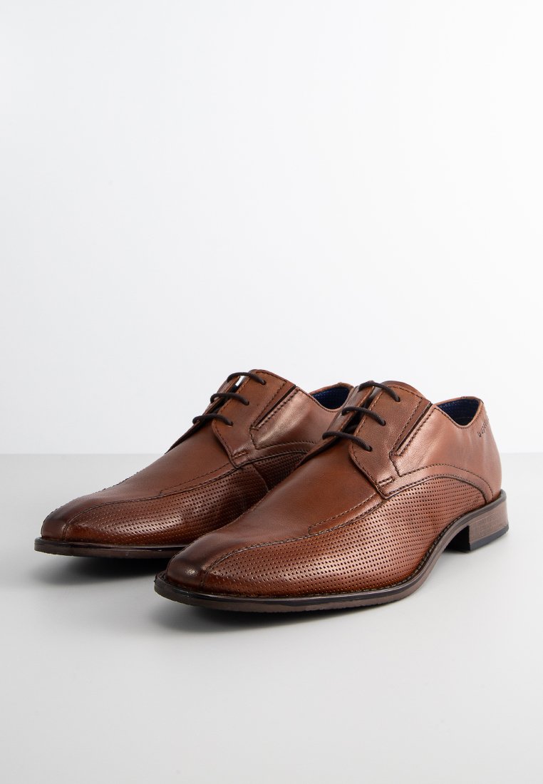 Par de zapatos de vestir para hombre de cuero marrón con detalles perforados y cordones negros sobre una superficie y fondo blancos.