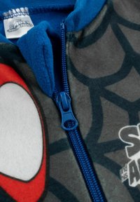 Tuta grigia in pile con accenti blu, caratterizzata da un motivo a ragnatela e una grande grafica rossa e bianca, con chiusura a zip visibile.