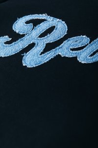Black fabric featuring light blue, frayed denim lettering spelling "Red," with curved, stylized design elements.