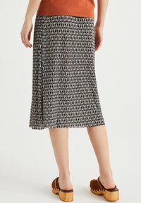 Black and white patterned skirt with a flared design. A solid orange top, wooden platform shoes, and a subtle hemline are visible.