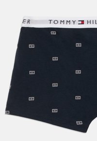 Tumed sinised bokserid valge vöökohtadega, millel on tekst "Tommy Hilfiger" ja väiksed valged ristkülikukujulised logo mustrid, mis on kangale hajutatud.