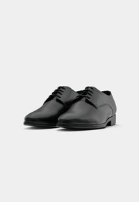 Schwarze Leder-Dressschuhe mit glatter Oberfläche, spitz zulaufender Zehenform und genähten Details. Sie verfügen über einen niedrigen, rechteckigen Absatz und ein Schnürdesign.