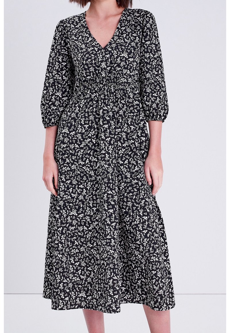 Robe noire à imprimé floral avec décolleté en V, manches bouffantes et taille ajustée qui s'évase en jupe midi en tissu léger.
