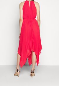 Vestido de halter plisado en rosa brillante con dobladillo asimétrico; presenta una espalda con abertura, cintura ajustada y se acompaña de sandalias de tacón metálicas.