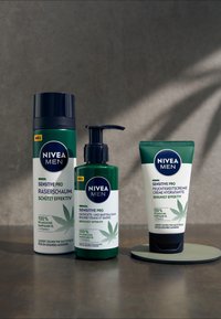 Three NIVEA MEN Sensitive Pro products: a dark blue canister of shaving foam, a green pump bottle for facial and beard balm, and a white tube for moisturizer, all featuring leaf accents.