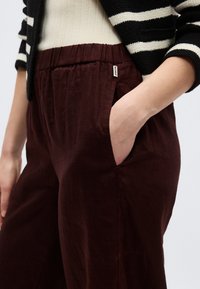 Hand in pocket of dark brown elastic waist pants worn with white top and black-and-white striped knit cardigan.