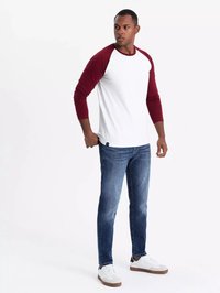 Weißes Langarmshirt mit weinroten Raglanärmeln, kombiniert mit blauen Jeans und weißen Sneakern. Das Shirt hat ein Rundhalsausschnitt-Design.