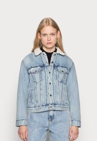 Lichtblauwe denimjack met een zachte, crèmekleurige fleece kraag, sluiting met knopen aan de voorkant en twee borstzakken. Distressed details aanwezig.