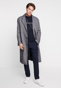 Grå ullblandingskåpe med skreddersydd design, lange ermer og notched revers, kombinert med en marineblå t-skjorte og matchende bukser.