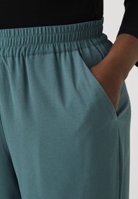 Teal joggingsbyxor med elastisk midja, sidofickor och ett strukturerat tyg för komfort och rörelsefrihet.