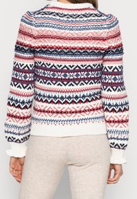 Pull en tricot présentant des motifs multicolores en rouge, bleu et blanc. Col et poignets côtelés, avec une coupe courte et un tissu texturé.