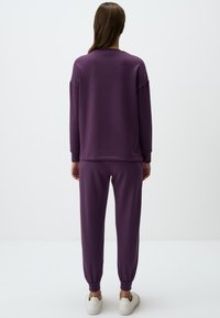 Felpa viola e joggers abbinati realizzati in tessuto morbido, con maniche lunghe, vestibilità comoda, polsini elasticizzati e sneaker bianche.