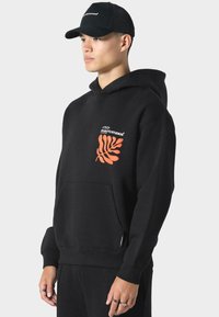 Černá mikina s kapucí z bavlny, s klokankou, s oranžovým grafikou listu na levé části hrudníku. Doplněno černou kšiltovkou.