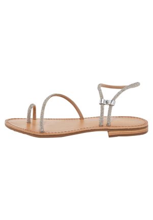 Flat sandal with a tan leather sole and decorative silver straps. Features a minimalist design with thin bands and a delicate buckle detail.