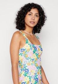 Vestido sem mangas floral com uma mistura de flores amarelas, rosas e azuis sobre um fundo branco, com decote quadrado e silhueta ajustada.