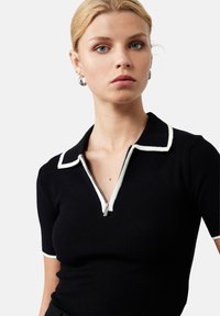 Zwart polo shirt met korte mouwen, voorzien van een witte kraag en een rits. De stof is geribbeld en heeft contrasterende accenten bij de kraag en de uiteinden van de mouwen.