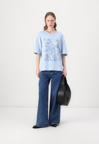 Light blue oversized t-shirt featuring a floral print, paired with wide-leg blue jeans and carrying a black tote bag.