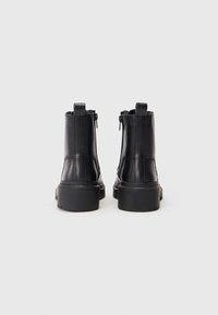 Botas de tobillo de cuero negro con una textura suave, suelas de goma gruesa y cremalleras laterales. Incluyen lengüetas en la parte posterior para facilitar su puesta.