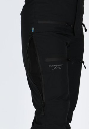 Zwarte broek gemaakt van duurzame stof met ritsen aan de zijkanten, een klein accent van de Zweedse vlag en een "SWEDEMOUNT" logo nabij de heup.