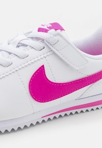Baskets blanches avec une finition en cuir texturé, arborant un logo swoosh Nike rose vif et des accents roses sur la semelle et la languette.