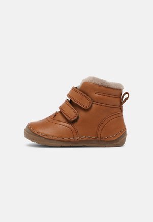 Botte marron pour tout-petit avec deux sangles velcro, doublure douce en fourrure, semelle cousue et languette au talon sur fond blanc.
