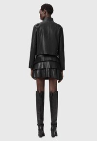 Μαύρο δερμάτινο τζάκετ με κομμένη σχεδίαση, διαθέτει επιφάνειες στους ώμους. Συνδυάζεται με φούστα πλεχτή σε μαύρο χρώμα με επίπεδα και μπότες έως το γόνατο.