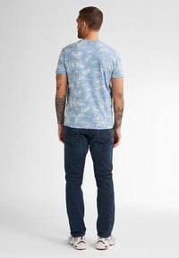 Světle modré tričko s krátkým rukávem zdobené bílým květinovým vzorem, spárované s tmavými džíny a bílými teniskami.