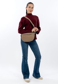 Hnědá kožená kabelka přes rameno s nastavitelným popruhem, zaobleným tvarem, kovovým zipem a hladkým texturovaným povrchem.