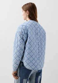 Jachetă căptușită albastră cu un model în diamant, cu margine rotundă și manșete ribbate. Fabricată dintr-un material ușor cu o textură moale.