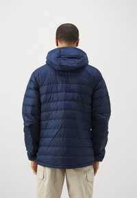 Námornícka modrá nafúknutá bunda s kapucňou, s prešívanými časťami a hladkým povrchom. Dizajn obsahuje elastické manžety a mierne zakrivený lem.