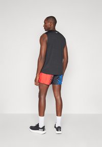 Svart ärmlös topp, röd och blå mönstrade shorts, svarta sneakers med vita detaljer och vita sportstrumpor.