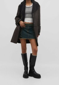 Cappotto di suede nero con un ampio colletto, maglione grigio a maglia, mini gonna di denim e alti stivali di gomma neri con suole spesse.