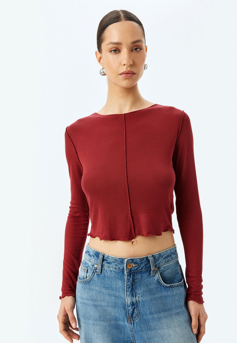 Burgundy långärmad crop top med rund halsringning och vågig kant, tillverkad av ribbat material; kombinerad med ljusblå högmidjade jeans.