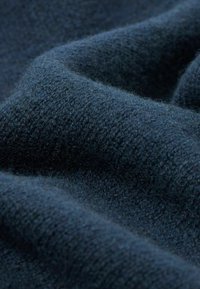 Dunkelblauer Wollstoff mit einer weichen, strukturierten Oberfläche, die sanfte Falten aufweist, welche die Wärme und Dichte des Materials betonen.