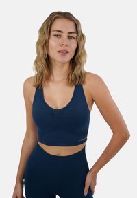 Top sportivo blu navy con dettaglio arricciato sul davanti e spalline larghe. Realizzato in tessuto liscio, abbinato a leggings aderenti coordinati.