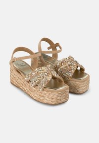 Sandali wedge beige con base in juta intrecciata, decorati con gemme scintillanti e numerose cinghie. La soletta liscia e lucida aggiunge un contrasto.