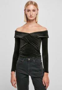 Svart off-the-shoulder topp i myk, ribbet stoff med lange ermer og vridd frontdesign, kombinert med mørke jeans.