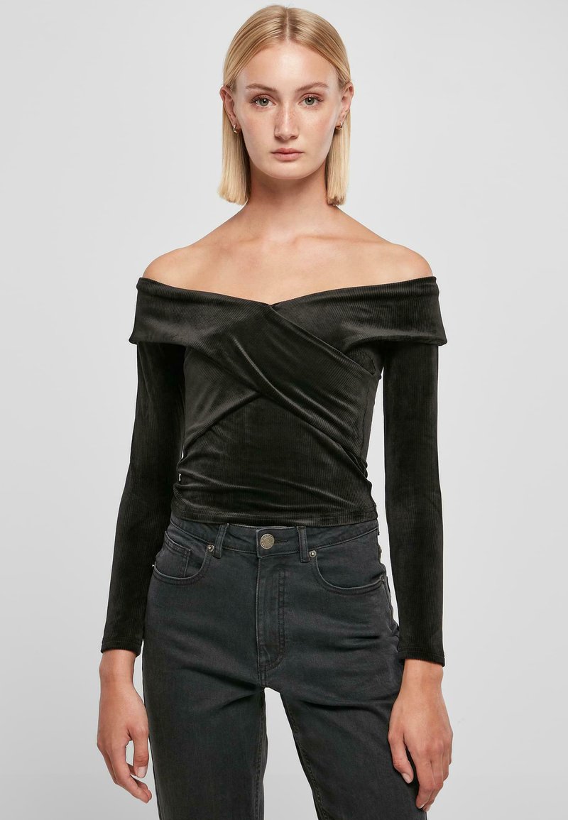 Svart off-the-shoulder topp i myk, ribbet stoff med lange ermer og vridd frontdesign, kombinert med mørke jeans.