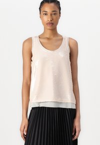 Beige paljett tanktopp med dyp hals og myk tekstur. Lagd over et gjennomsiktig grått stoff, kombinert med et svart plisserte skjørt.